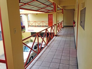 A corridor with a tiled floor, red railings, and a sign reading "SUNDECK SUITES WELCOMES YOU". - Sundeck Suites (Port of Spain)