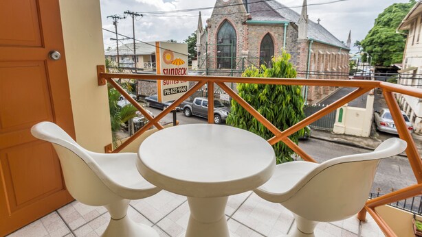 A balcony with two white chairs and a small round table, overlooking a street with a church and a signboard.
