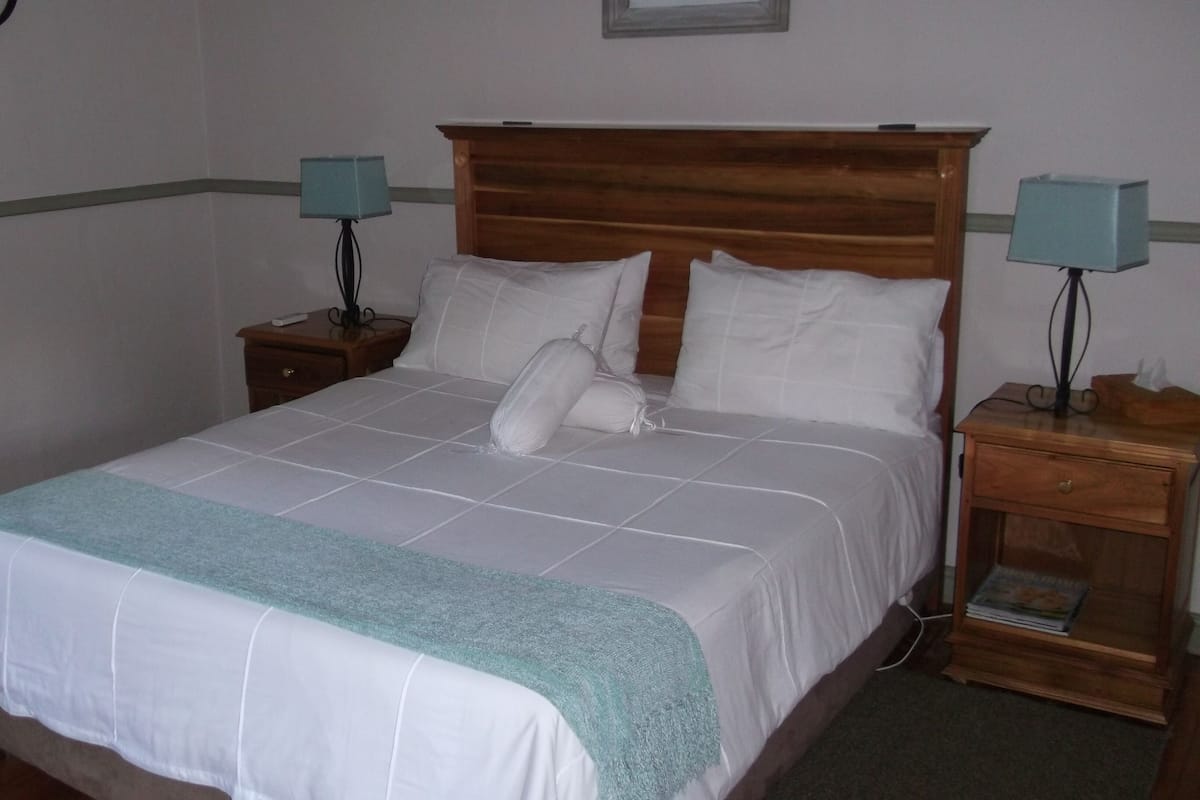 A neatly made bed with a wooden headboard, two bedside tables with lamps, and a nightstand with a magazine.