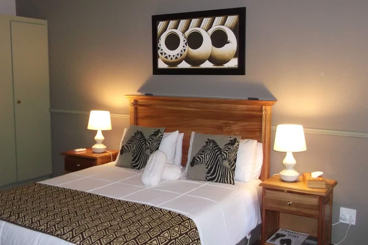 A neatly arranged hotel room with a large bed, two bedside tables with lamps, a wooden headboard, and zebra-themed pillows.