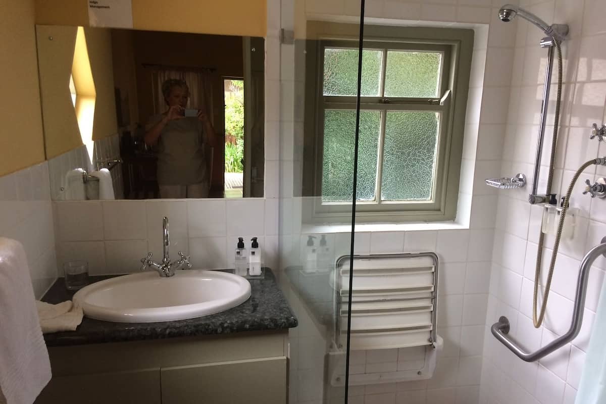 A bathroom with a sink, mirror, window, shower, and towel rack.