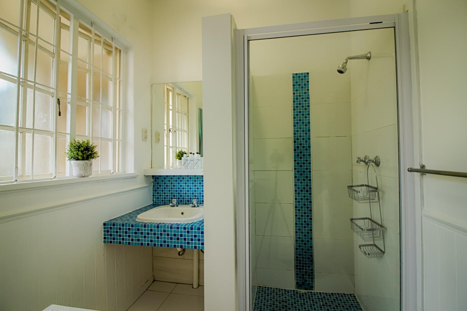 Un baño con ventana, lavabo, espejo, ducha y suelo de baldosas.