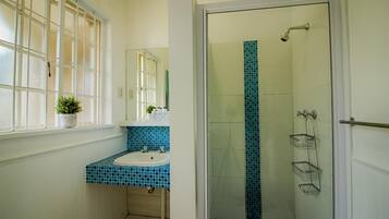 Un baño con ventana, lavabo, espejo, ducha y suelo de baldosas.