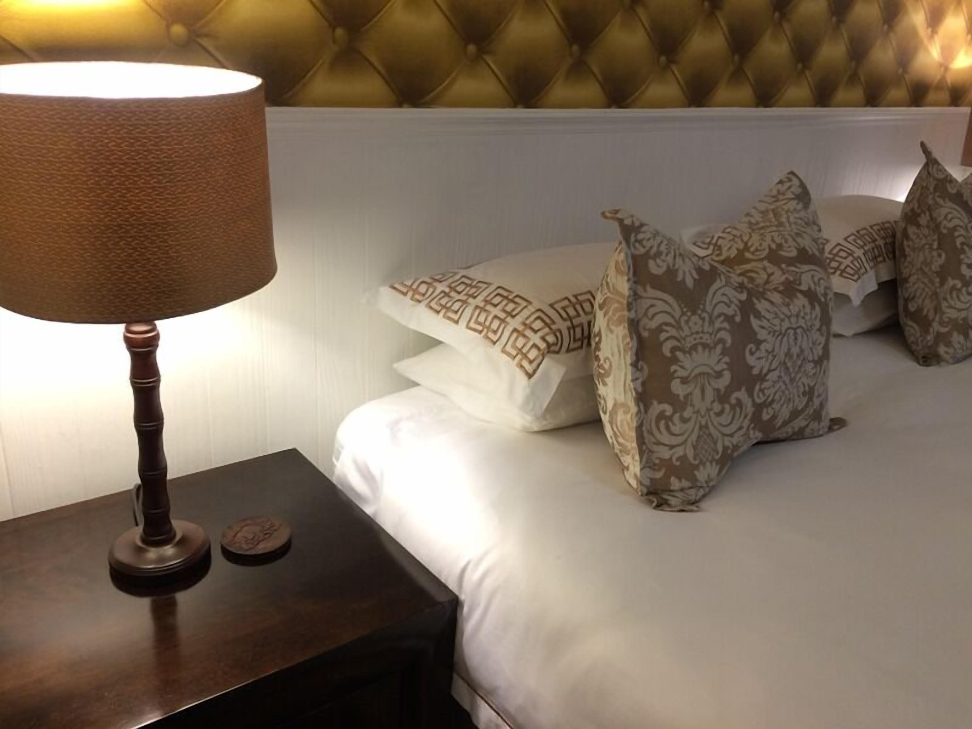 A hotel room with a tufted headboard, a bedside lamp, and patterned pillows.