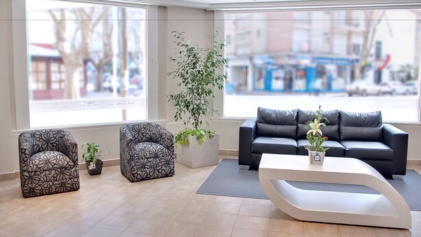Een moderne woonkamer met twee gestreepten fauteuils, een zwarte bank en een witte salontafel. Er is een groot raam met uitzicht op de straat en een potplant.