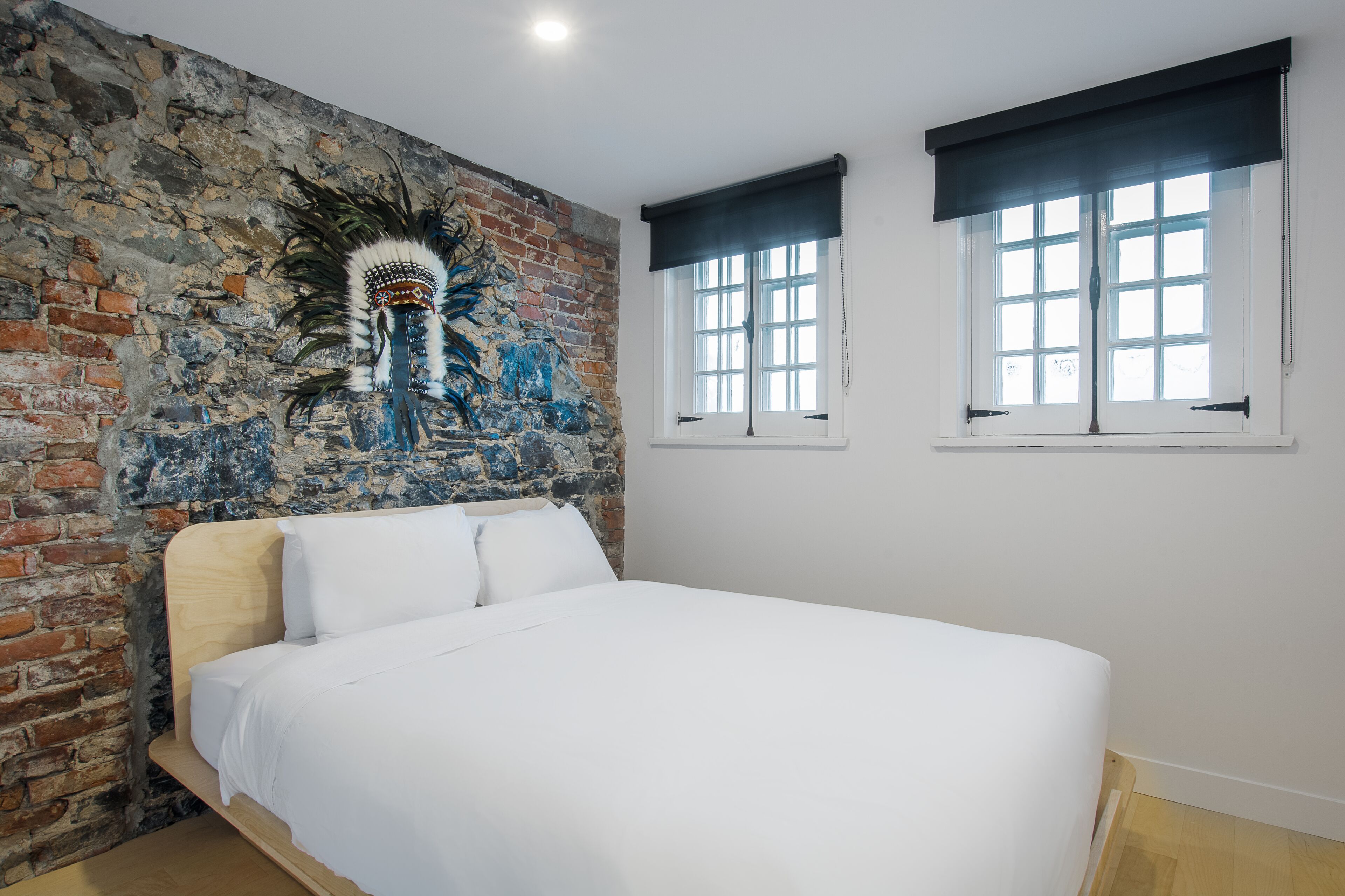 Un dormitorio con pared de ladrillo, una cama y dos ventanas con persianas oscuras.