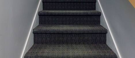 A staircase with carpeted steps and a wooden handrail, leading to a room with a light-colored wall and a visible door at the top.