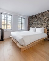 Un dormitorio moderno con una cama grande, dos ventanas, una pared de piedra y un calentador portátil.