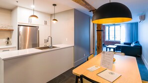 Une cuisine moderne dotée d’un réfrigérateur en acier inoxydable, de meubles blancs et d’un éclairage suspendu.