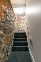 Una escalera con un rellano alfombrado y un muro de piedra a un lado.