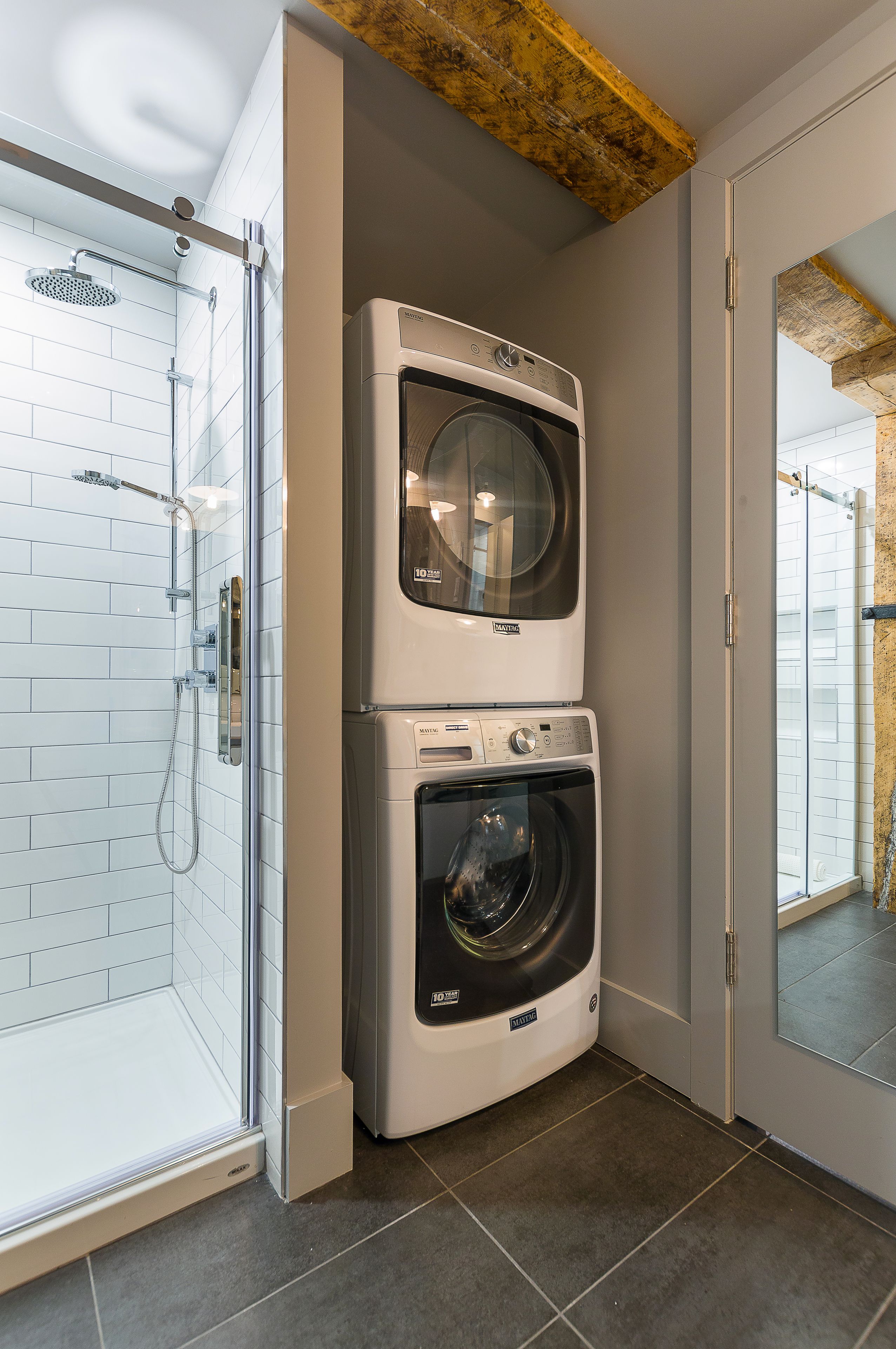 Une petite buanderie comprenant une douche fermée par une paroi de verre, un lave-linge à chargement par le haut et un sèche-linge à chargement frontal.