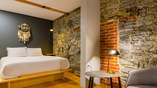 Une chambre à coucher avec un lit, une petite table avec une lampe et un mur en briques.