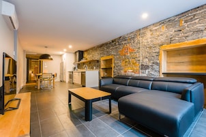 Una sala de estar moderna con un sofá de cuero negro, una mesa de centro de madera y una pared de piedra.