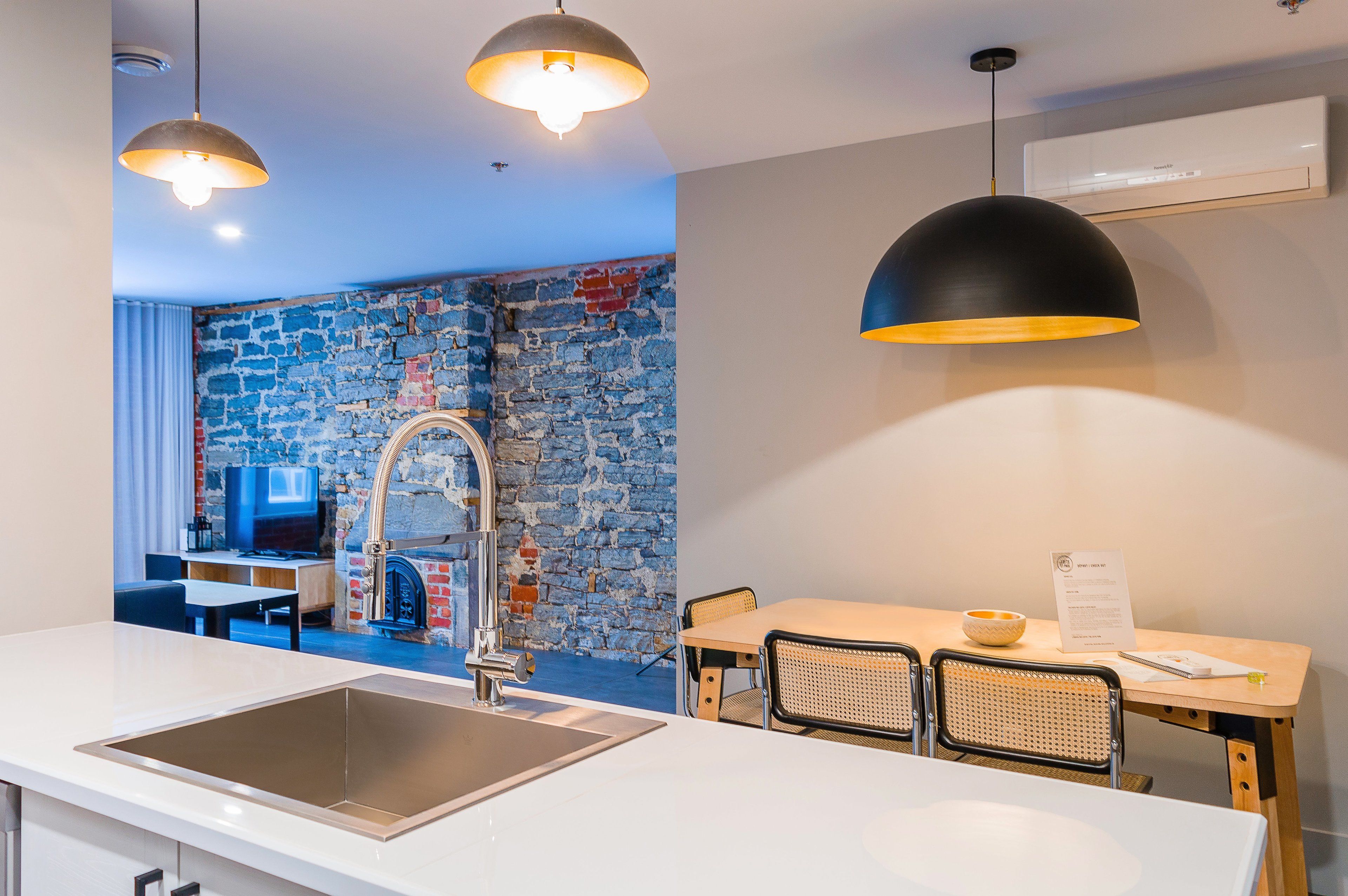 A modern kitchen with a stone wall backsplash, a stainless steel sink, and a dining area with a table and chairs.
