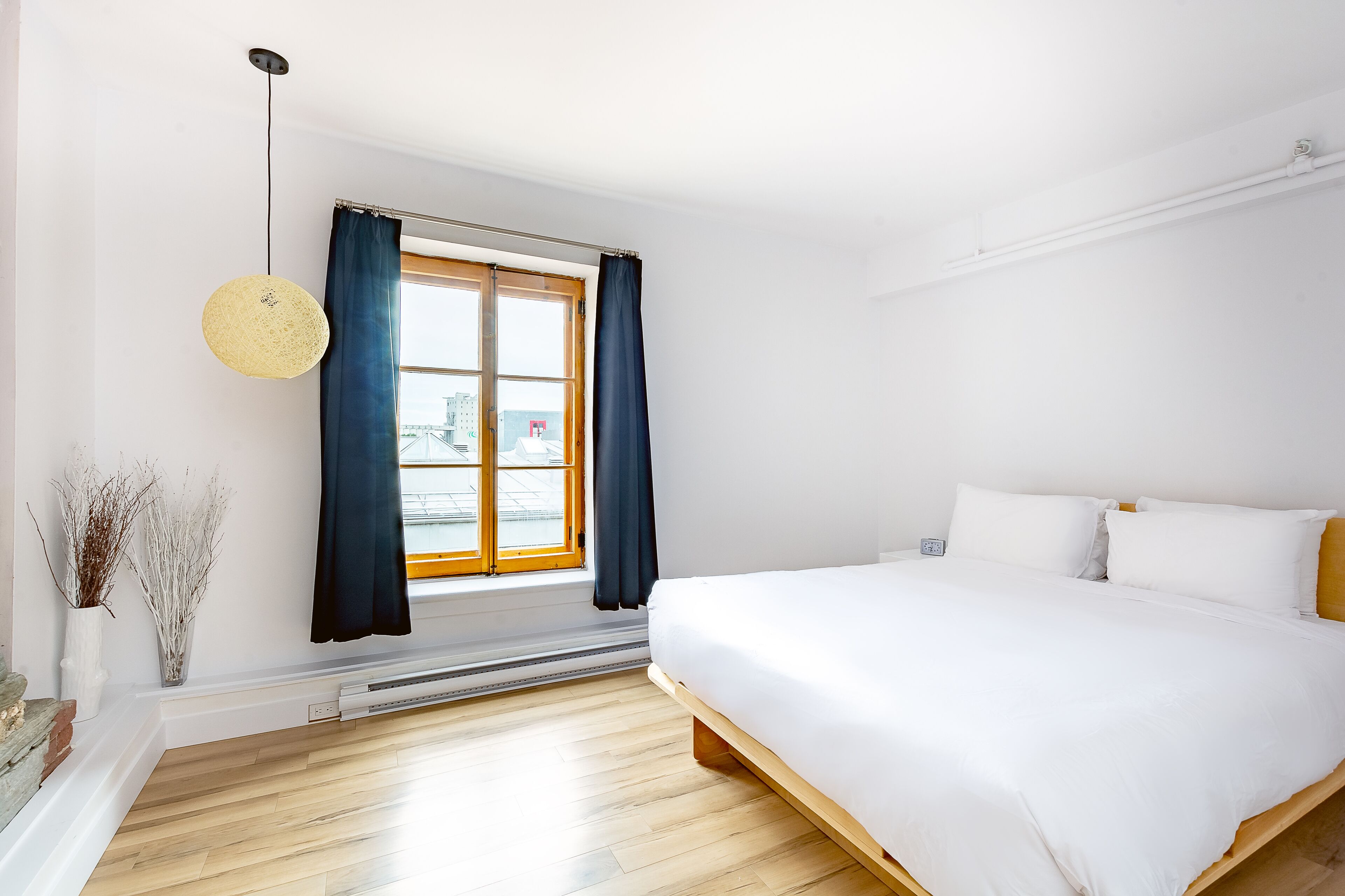 Ein modernes Schlafzimmer mit einem großen Bett, einem Fenster mit Vorhängen, einer Pendelleuchte und einer Heizung.