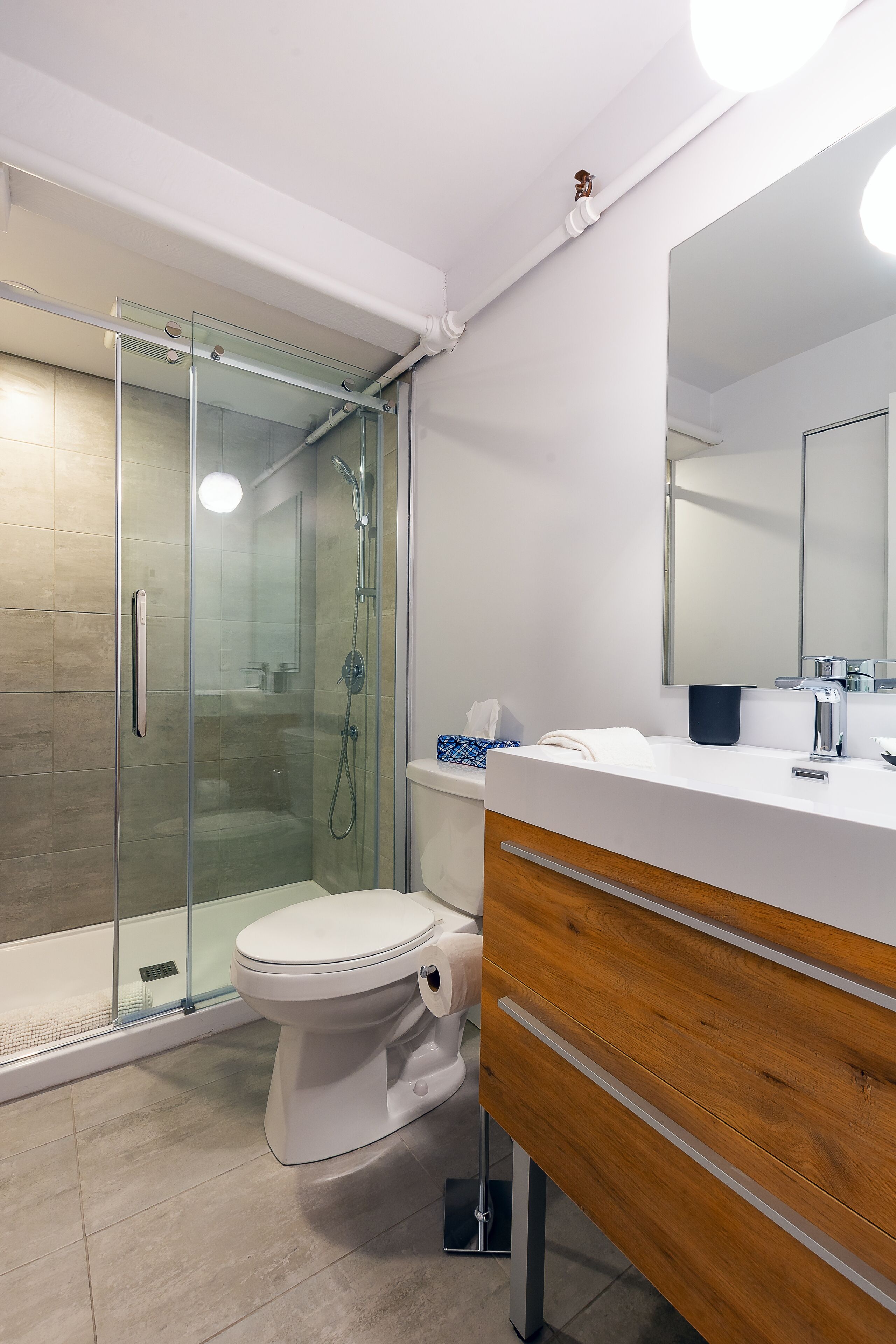 Une salle de bain moderne avec une douche à parois de verre, des toilettes blanches et un meuble-lavabo en bois avec un miroir.