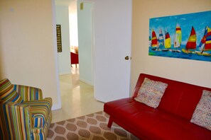 A room with a red sofa, a striped armchair, and a painting of sailboats on the wall.