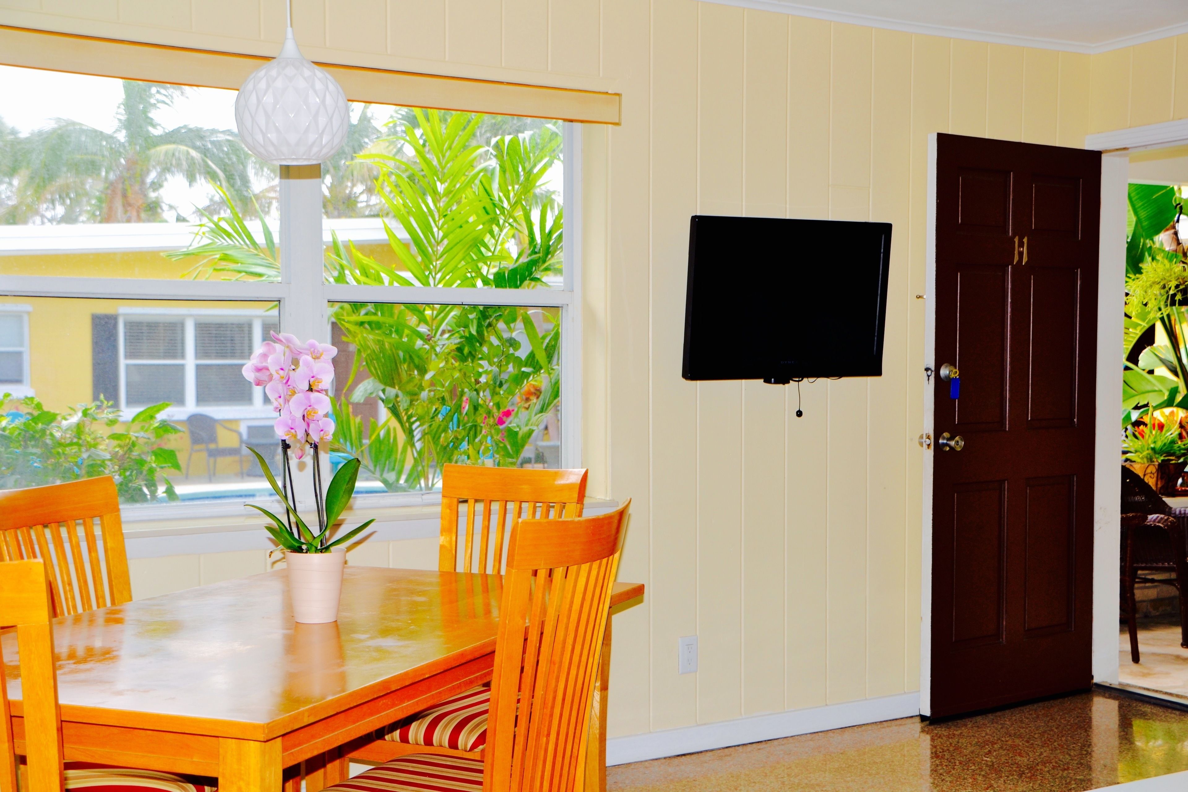 A dining area with a wooden table and chairs, a potted orchid, and a television mounted on the wall.