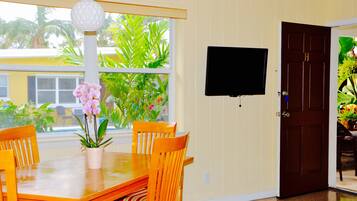 A dining area with a wooden table and chairs, a potted orchid, and a television mounted on the wall.