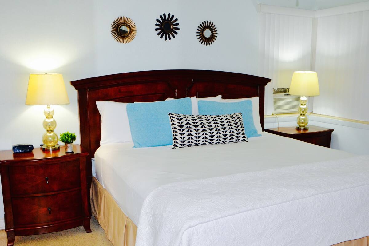 A neatly made bed with white linens, a wooden headboard, and two decorative wall mirrors.