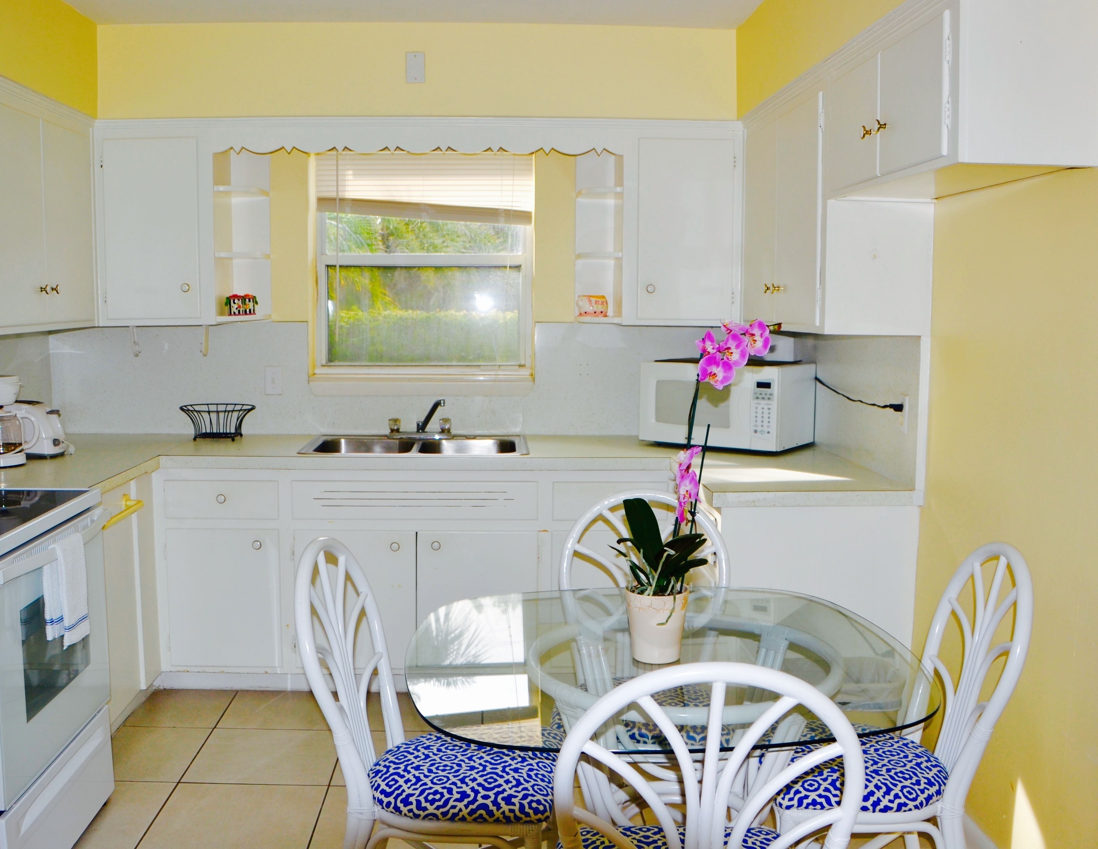 Cocina compacta con armarios blancos, microondas, pileta y una mesa de comedor con sillas.