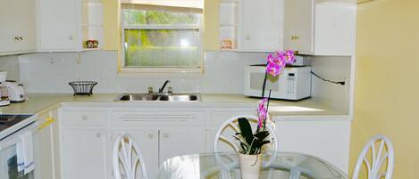 Cocina compacta con armarios blancos, microondas, pileta y una mesa de comedor con sillas.