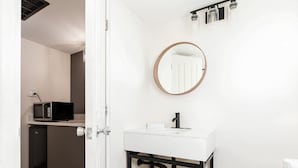 Un baño moderno con un lavamanos blanco, estructura de metal negro y un espejo redondo.