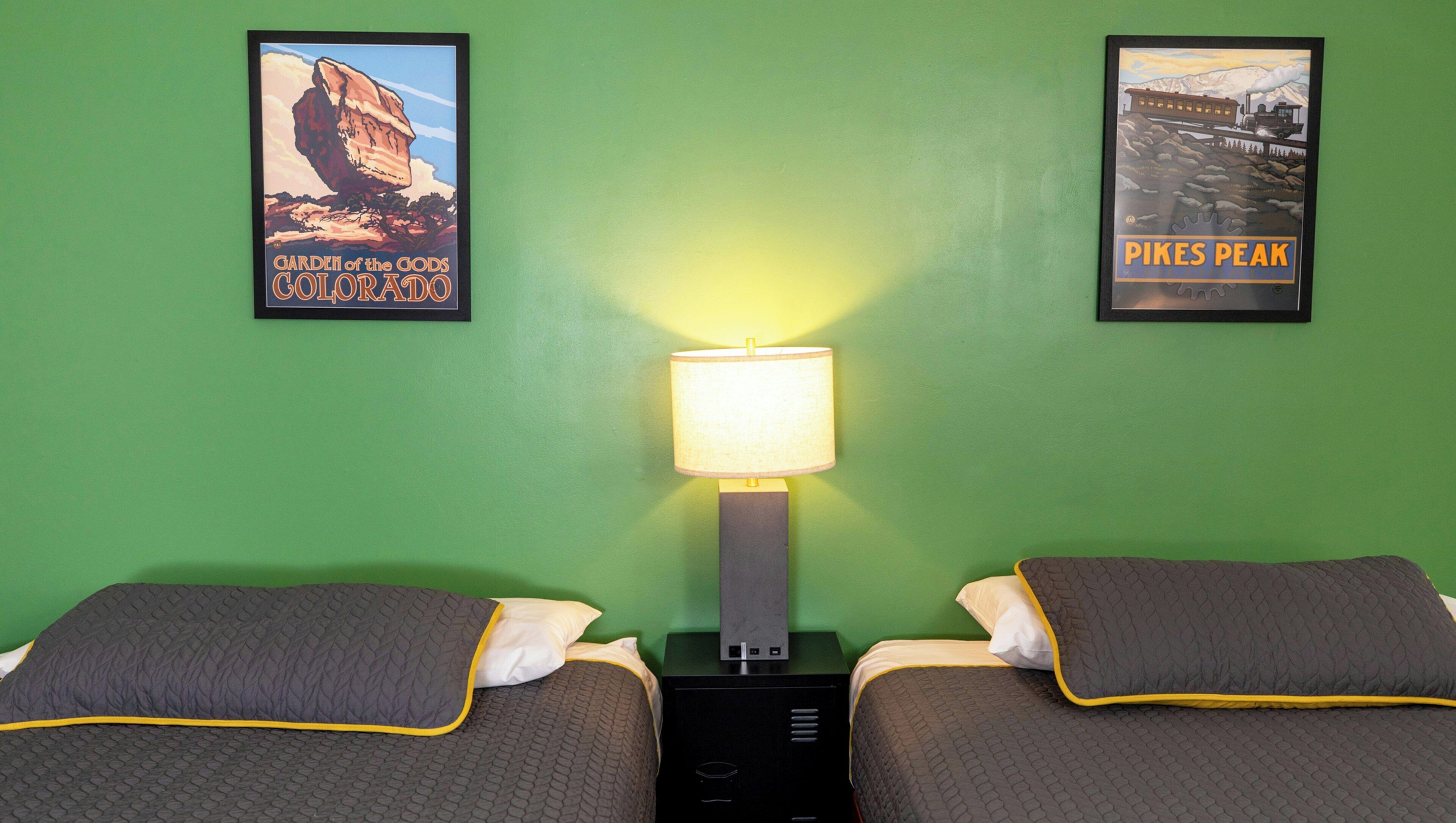 A room with two beds, a nightstand with a lamp, and two framed posters on the wall.