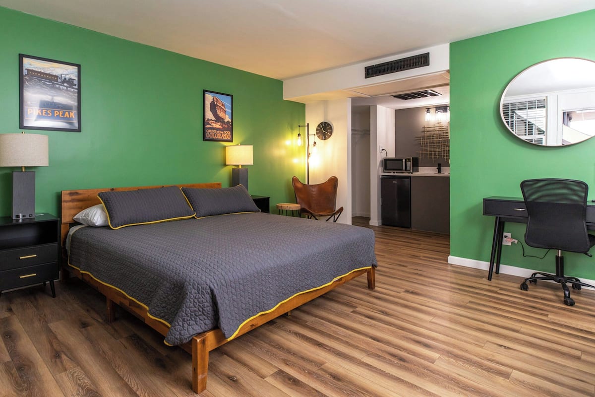 Une chambre à coucher avec un lit, un bureau, une chaise, une lampe, une horloge et une affiche accrochée au mur.