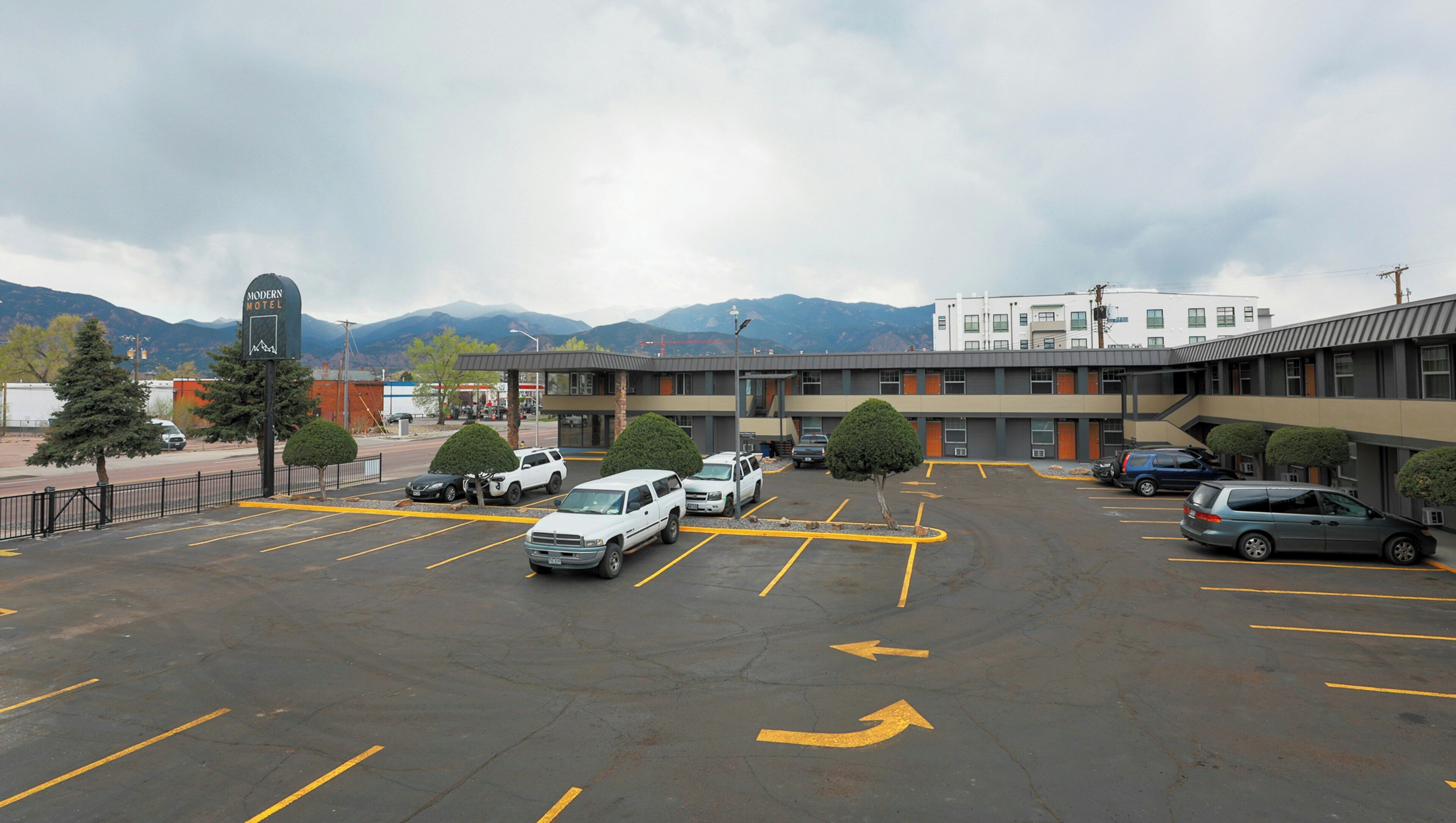 A parking lot with several cars, a motel building, and mountains in the background.