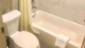 A bathroom with a toilet, a bathtub, and a shower curtain. - North Villa Inn (Houston)