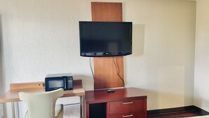 A hotel room with a flat-screen TV mounted on a wooden panel, a microwave on a wooden desk, and a chair. - North Villa Inn (Houston)