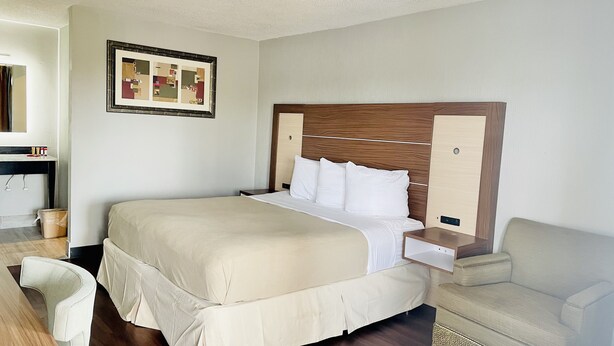 A neatly arranged hotel room with a large bed, a bedside table, a chair, and a small table with a mirror. - North Villa Inn (Houston)