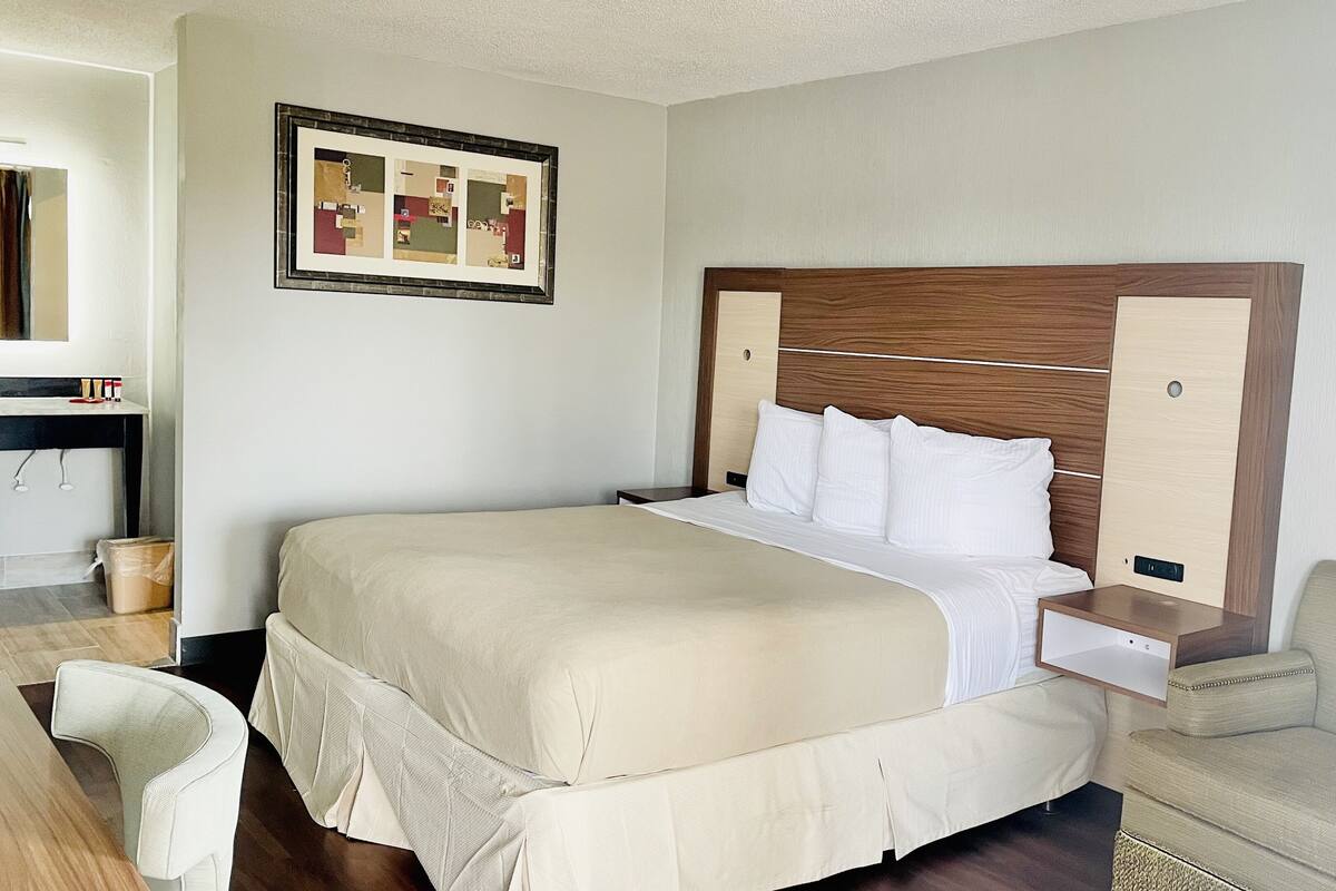 A neatly arranged hotel room with a large bed, a bedside table, a chair, and a small table with a mirror.