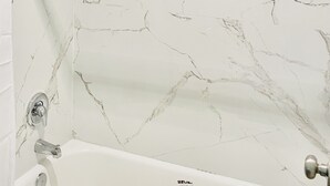 A bathroom with a bathtub, a shower, and a glass-enclosed shower area. - North Villa Inn (Houston)