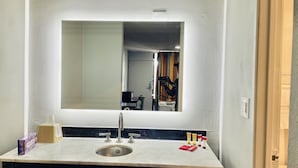 A bathroom with a large mirror, a sink, and toiletries. - North Villa Inn (Houston)