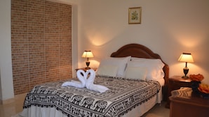 A neatly made bed with a patterned bedspread and two white towels arranged in a heart shape. There are two bedside tables with lamps, a wooden headboard, and a picture on the wall. - Caraná (Montenegro)