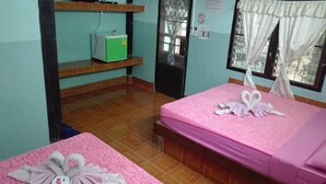Camera d'albergo con due letti, ciascuno con biancheria rosa e asciugamani a forma di cigno. C'è una televisione su un ripiano sopra i letti e un piccolo mobiletto verde sotto.