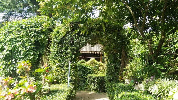 Un sentiero nel giardino conduce a un edificio rustico con tetto in legno e ringhiera decorativa.