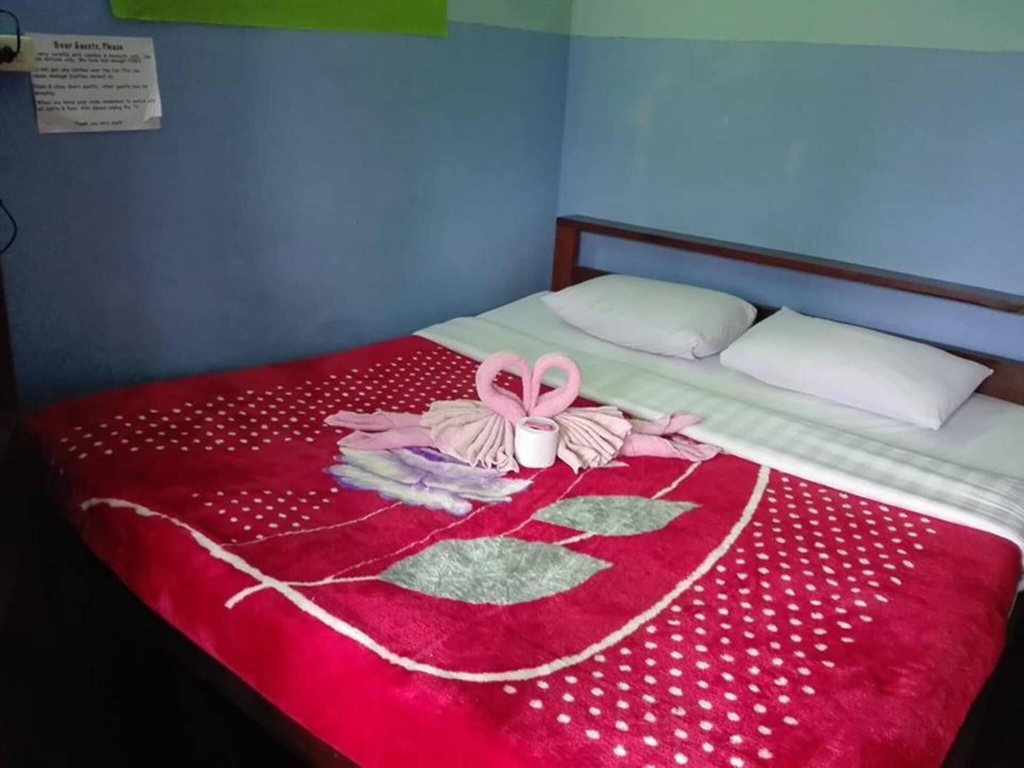Una cama bien hecha con una colcha roja y blanca de lunares, una toalla dispuesta en forma de corazón y una almohada blanca.