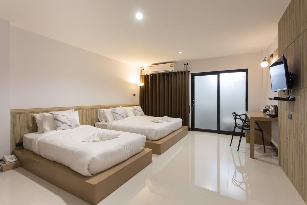 A hotel room with two beds, a desk, a chair, a TV, and a sliding door.