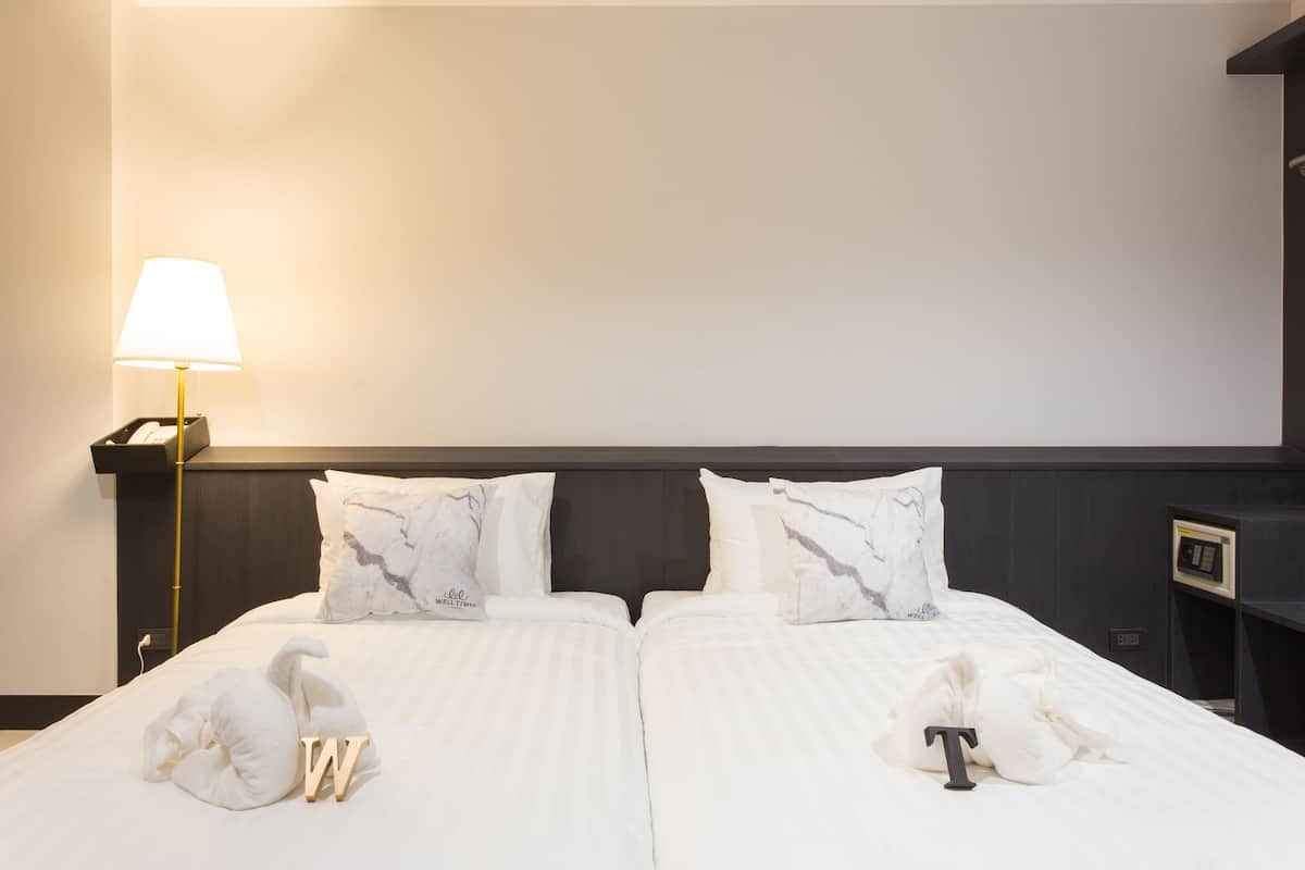 A hotel room with a bed, pillows, a lamp, and a nightstand.
