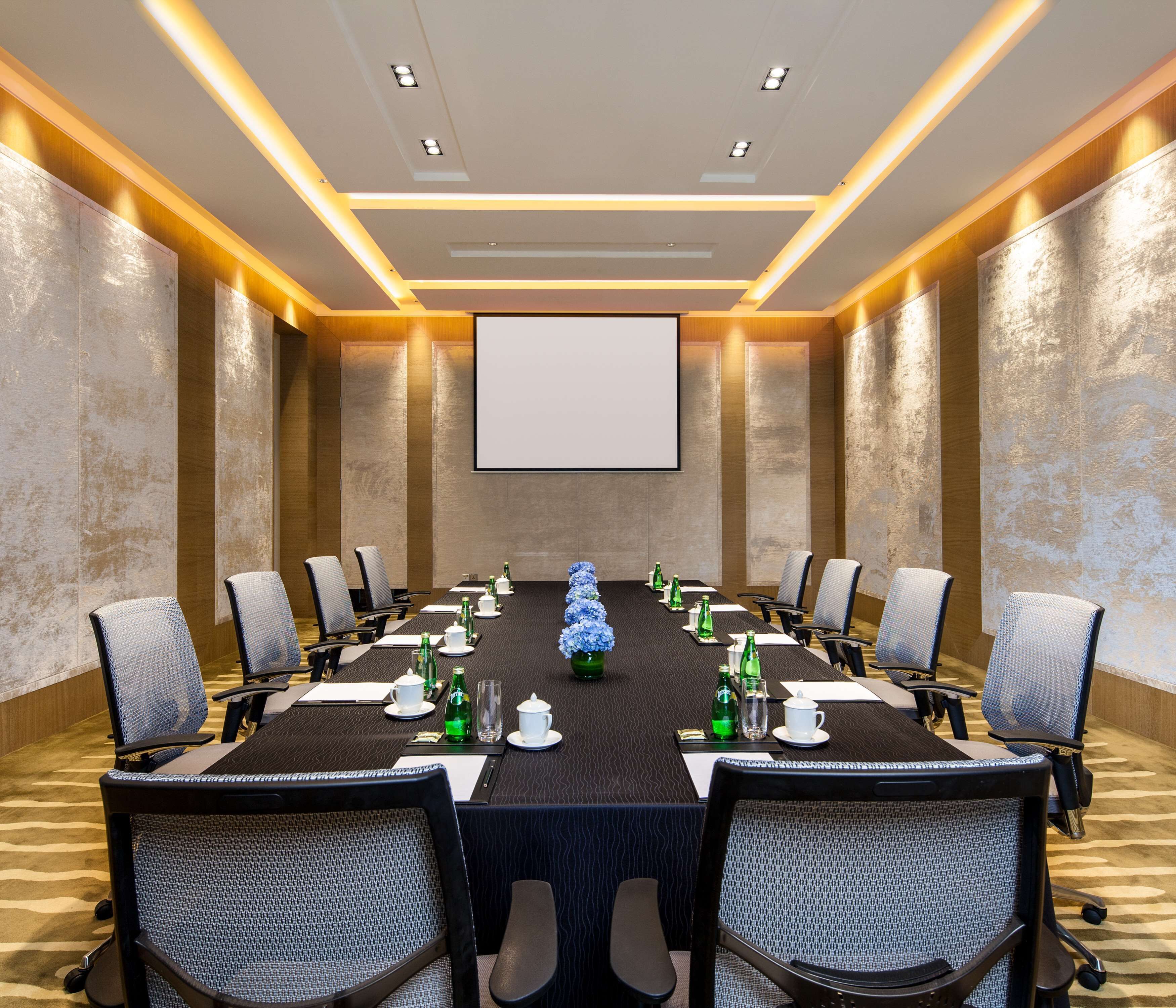 A conference room with a long table, chairs, a projector screen, and a floral centerpiece.