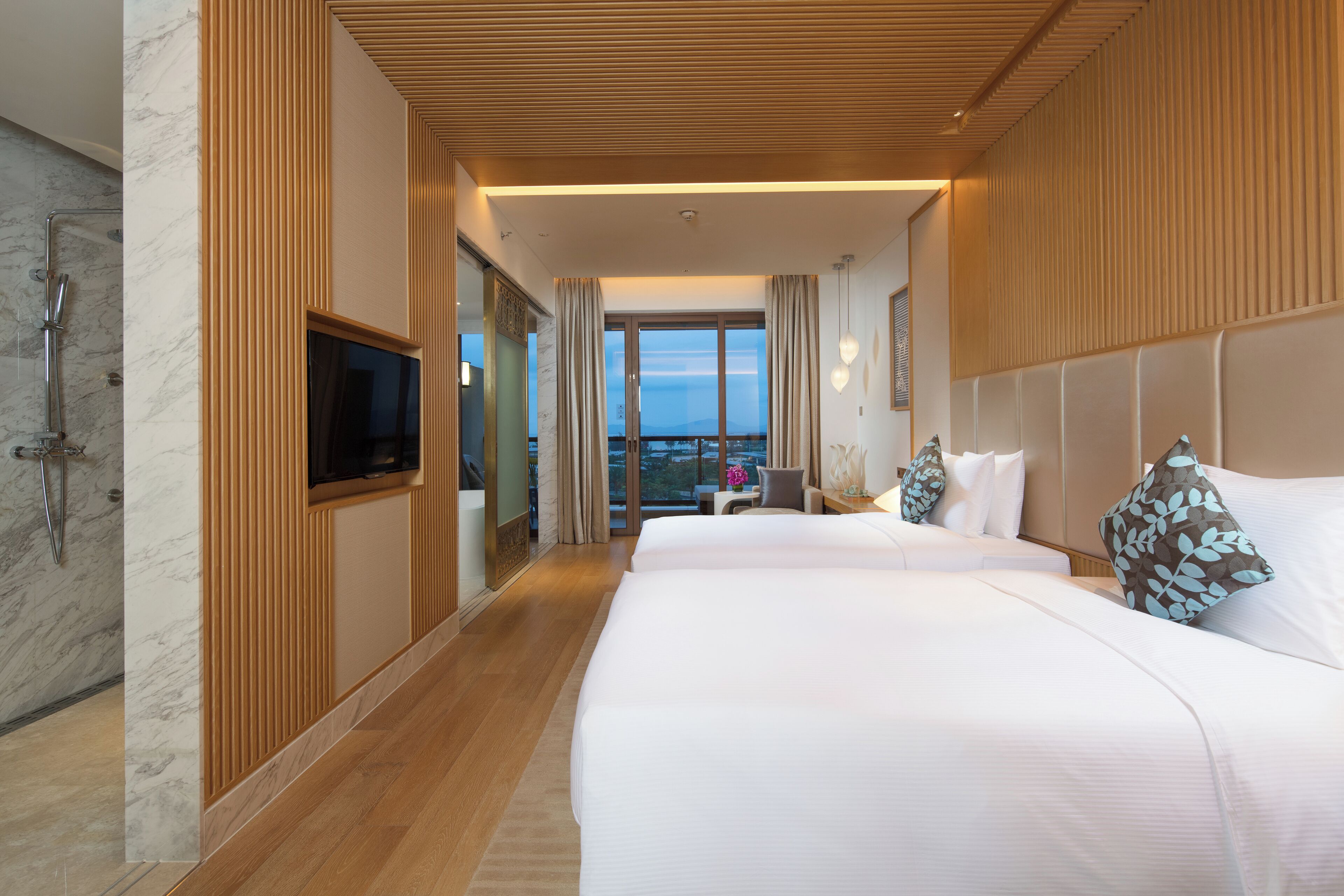 Ein Hotelzimmer mit einem großen Bett, einem Fernseher, einer Dusche und Blick auf die Stadt.