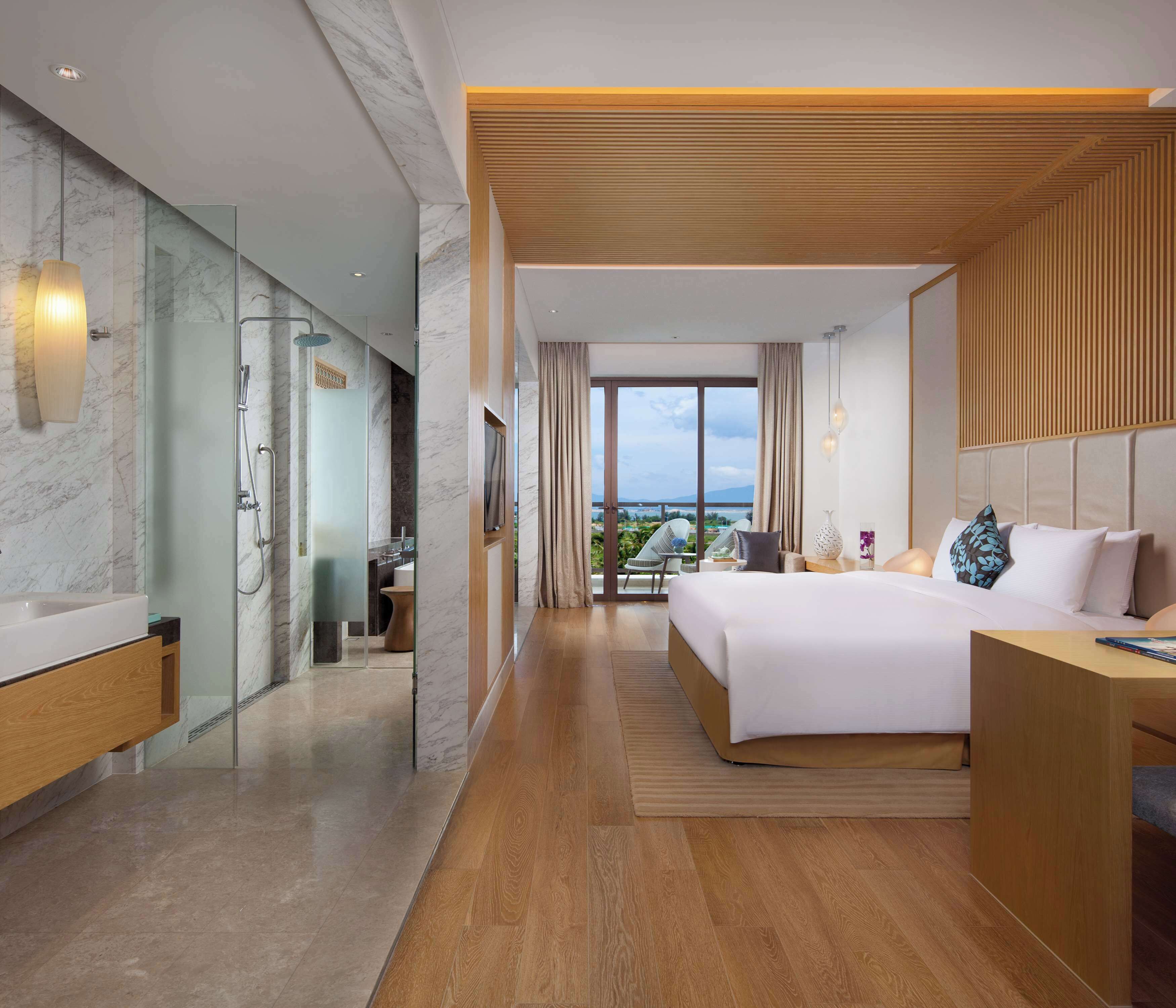 A modern hotel room with a large bed, a bathroom with a glass shower, and a view of the outdoors.