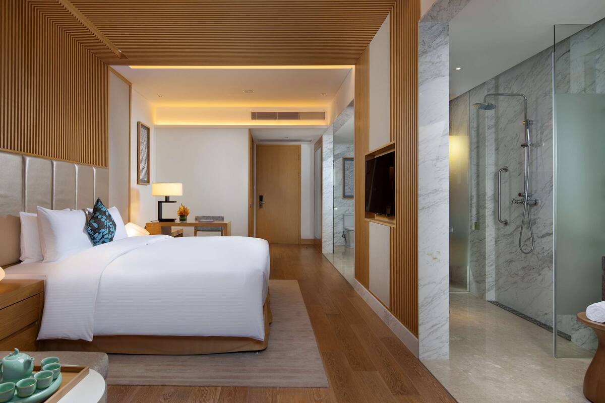 A modern hotel room with a large bed, bedside table, and a glass-enclosed shower area.