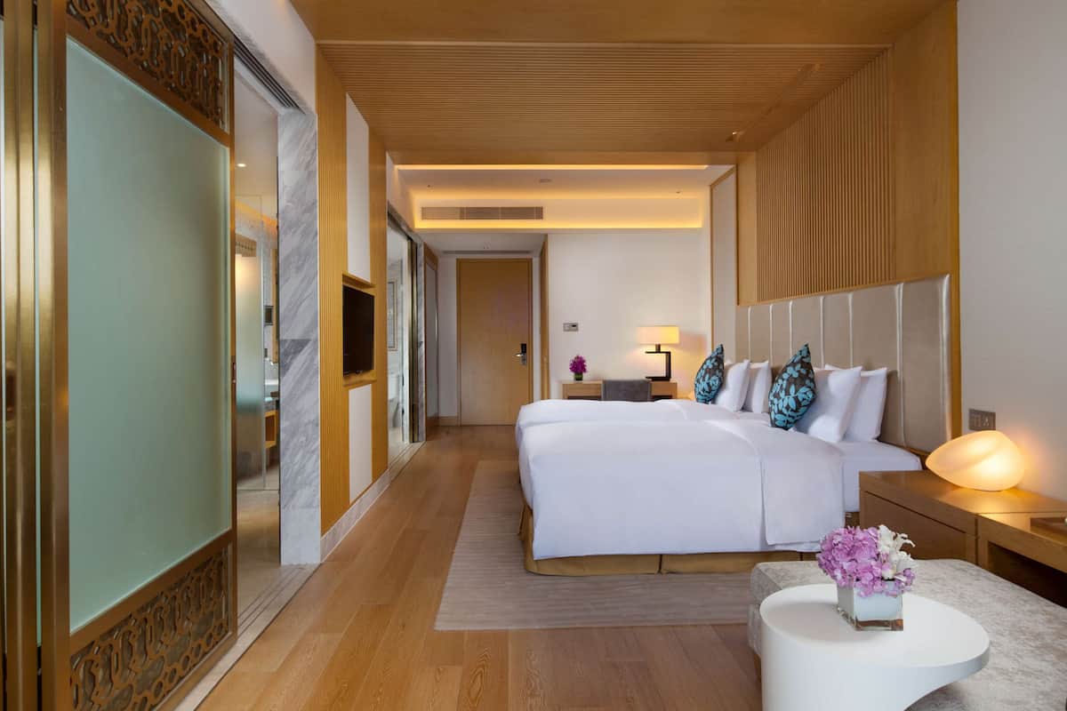 A modern hotel room with a large bed, bedside tables, a nightstand with a lamp, and a decorative vase.