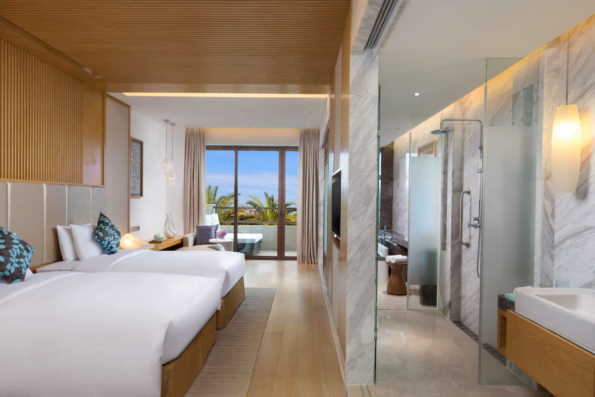 A hotel room with two beds, a balcony with a view, a shower area, and a bathroom with a marble countertop.