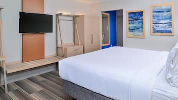 A hotel room with a bed, a TV mounted on the wall, a wardrobe, and two framed artworks on the wall.