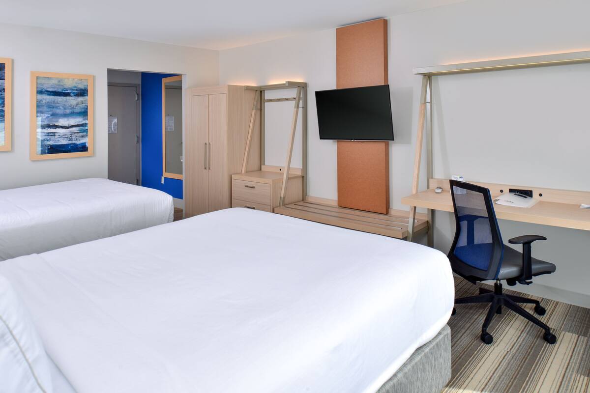 A hotel room with two beds, a desk with a chair, a TV, and a wardrobe.